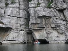 two people are in a small boat on the water near some large rocks and cliffs