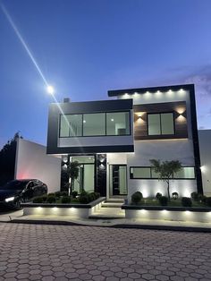 a modern house lit up at night with lights on the front and side of it