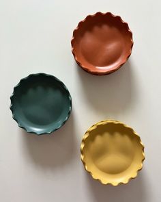 three different colored dishes on a white surface