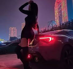 a woman standing next to a sports car in the city at night with neon lights