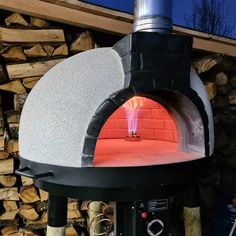 an outdoor pizza oven with flames coming out of it's sides and wood stacked in the background