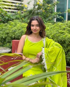 a woman in a green dress sitting on a bench with her arms crossed and looking at the camera