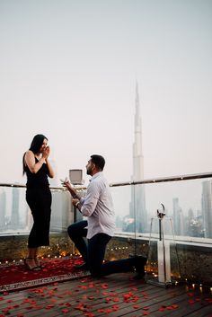 a man kneeling down next to a woman on top of a building