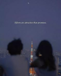 two people sitting on top of a building looking at the city lights and moon in the sky