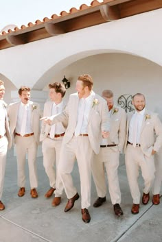 a group of men standing next to each other wearing white suits and tan ties on their wedding day