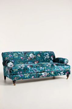 a blue floral couch with wooden legs on a white background in front of a wall