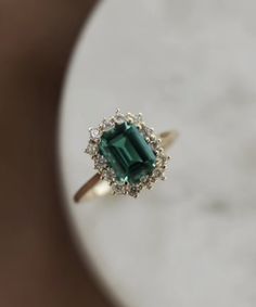 an emerald and diamond ring sitting on top of a table