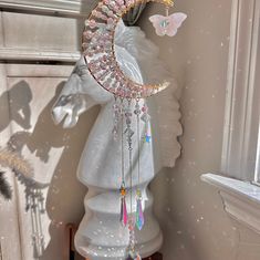 a white statue with a pink and gold necklace hanging from it's side next to a window