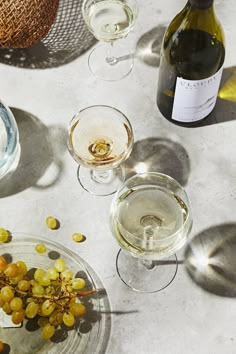 several wine glasses and bottles on a table with some grapes in the bowl next to them