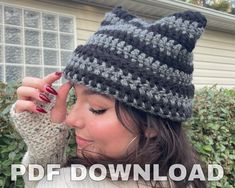 a woman wearing a knitted hat and mitt in front of a house with bushes