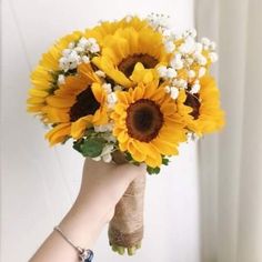 a hand holding a bouquet of sunflowers in front of a white wall and window