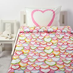 a bed with a heart pillow on top of it next to a night stand and nightstand