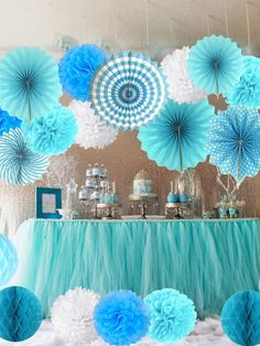 a dessert table with blue and white paper flowers, tissue pom poms, and other decorations