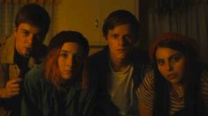 four young people are sitting together in the dark, one is looking at the camera