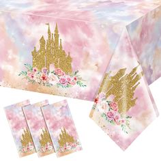 a table cloth with gold glitter castle on it and pink flowers in the center, along with matching napkins