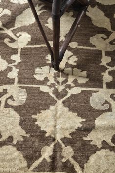 a brown and white area rug with an ornate design on the top, in front of a wooden chair