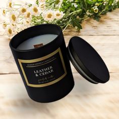 a black candle sitting on top of a wooden table next to white and yellow flowers