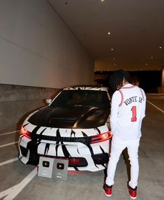 a person standing next to a white car with graffiti on it's hoodie