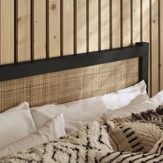 a bed with pillows and blankets on it next to a wooden headboard that has wood slats