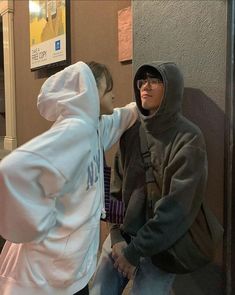 two people standing next to each other in front of a building wearing hoodies and sweatshirts