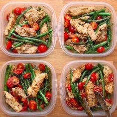 four plastic containers filled with chicken, green beans and cherry tomatoes on top of a wooden table