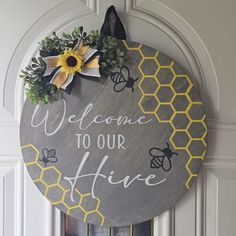 a welcome to our hive sign hanging on a door with flowers and bees around it