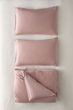 two pink pillows and one white pillow on a bed