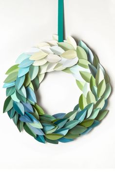 a wreath made out of paper leaves hanging from a green ribbon on a white wall