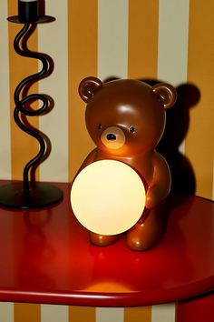 a brown teddy bear sitting on top of a red table next to a white light