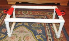 a white plastic table with red handles sitting on a rug in front of a bed