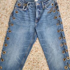 a pair of blue jeans with gold buttons on the bottom and side, sitting on a floor