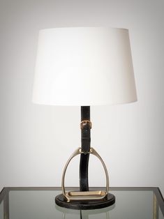 a lamp on a glass table with a white lampshade and black leather strap