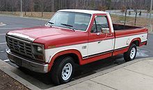 a red and white pickup truck parked in a parking lot next to a tree lined street