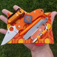 a person holding an orange and black knife in their hand with other items on it