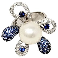 Ring size: 7.75 This marvelous pearl, diamond and sapphire cocktail ring is an absolute stunner! Whimsical yet luxurious, this sparkling ring offers vibrant color, a bold design and incredible dimension. The sizeable cocktail style ring features a large round South Sea cultured pearl surrounded by a 5 shimmering embellished 'petals' set with natural diamonds and dazzling sapphires. The design is 3 dimensional with actual full curved petals. This ring will fill your finger with sparkle and make a Sapphire Cocktail Ring, Sparkling Rings, Ring With Diamond, Diamond Cocktail Rings, Pearl Flower, Pearl Diamond, Bold Design, Natural Sapphire, Types Of Rings