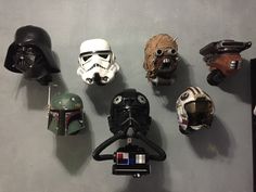 several star wars helmets are lined up on a gray wall, with one wearing a helmet