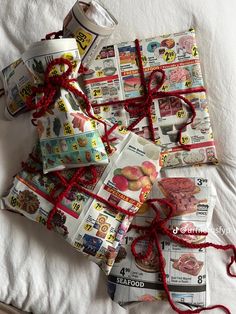 several wrapped packages with red string on top of a white bed covered in newspapers and magazines