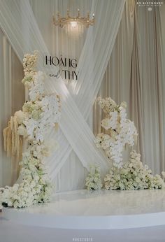 a wedding cake with white flowers on it and a chandelier hanging from the ceiling