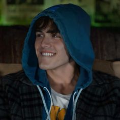 a young man wearing a blue hoodie smiles at the camera while sitting in a chair