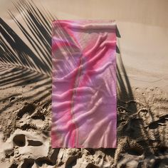 a towel laying on top of a sandy beach next to a palm tree leaf shadow