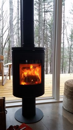 a fire burning inside of a stove in a living room next to a large window