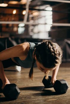 a woman doing push ups with two black dumbbells on the floor in a gym