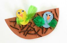 two paper birds sitting on top of a piece of wood with grass and feathers around them