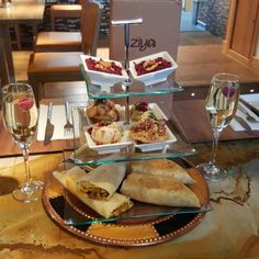 three tiered glass plate with food on it and two glasses of wine next to it