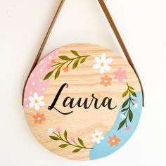 a wooden sign hanging on the wall that says laura with flowers and leaves painted on it