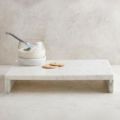 a white table with crackers and a bowl on it, in front of a concrete wall