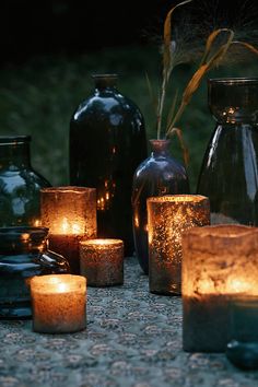 many lit candles are on the ground next to vases and glass bottles with plants in them