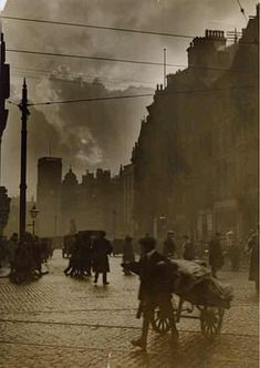 an old photo of people and horses on a cobblestone street with buildings in the background