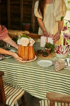 two women are decorating a cake with flowers on it at a table in front of them