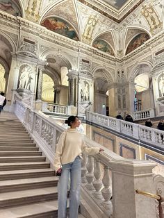 a woman is standing on the stairs in a building with ornate ceilings and painted walls